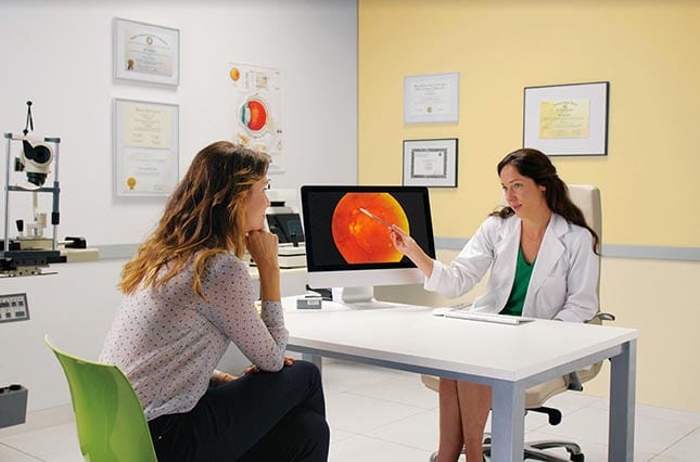 A female doctor points at something on a screen while sitting with a patient.