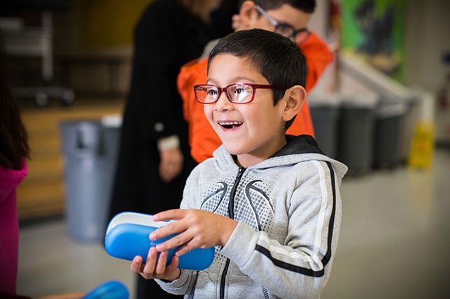 A young boy smiles while wearing a new pair of glasses and holding a blue glasses case.